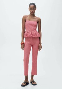 Red gingham peplum top with thin straps paired with slim-fit red gingham pants. Black flip-flops and stacked orange bracelets complete the look.