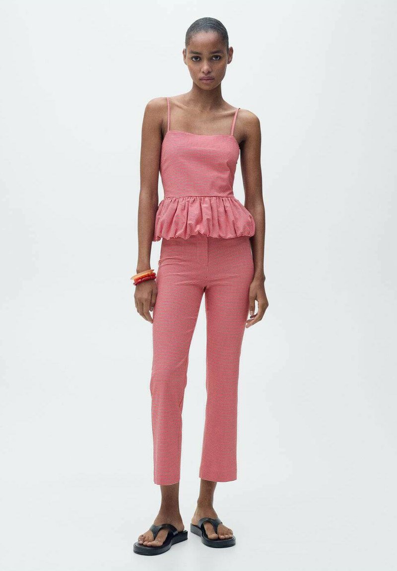 Red gingham peplum top with thin straps paired with slim-fit red gingham pants. Black flip-flops and stacked orange bracelets complete the look.