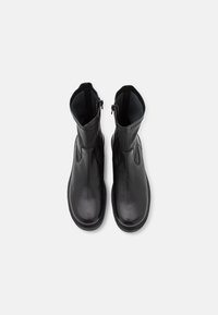 Bottes chevilles en cuir noir à texture lisse, fermeture éclair latérale et design à bout rond. Semelle souple pour plus de confort.