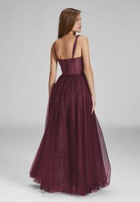 Robe de soirée bordeaux avec un corsage ajusté et des bretelles fines. Dotée d'une jupe fluide en tulle scintillant qui descend jusqu'au sol.