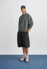 Sweatshirt vert foncé, shorts noirs et baskets grises. Caractéristiques : coupe décontractée, poignets côtelés et accents du logo Nike. Design simple et fonctionnel.