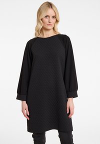 Schwarzes Kleid mit einem strukturierten Muster, Raglanärmeln und lockerer Passform. Das Material wirkt weich und bequem, geeignet für die Freizeit.