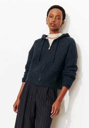 Sweat à capuche court bleu marine foncé en maille texturée, doté d'une fermeture éclair frontale, de cordons de serrage et de manches longues, associé à un pantalon à fines rayures.