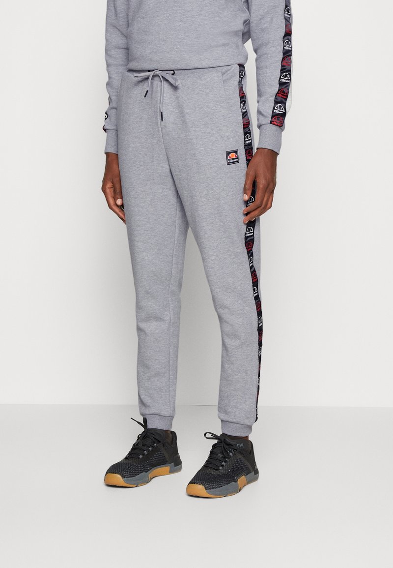 Grijze sweatpants met een elastische tailleband en een trekkoord, zijstrepen in een donkere kleur met logo-patronen, en een taps toelopend ontwerp.