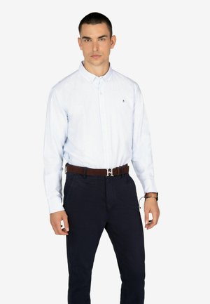 Camisa de botón a rayas azul claro con cuello, combinada con pantalones azul marino oscuros y un cinturón marrón con una hebilla de plata.