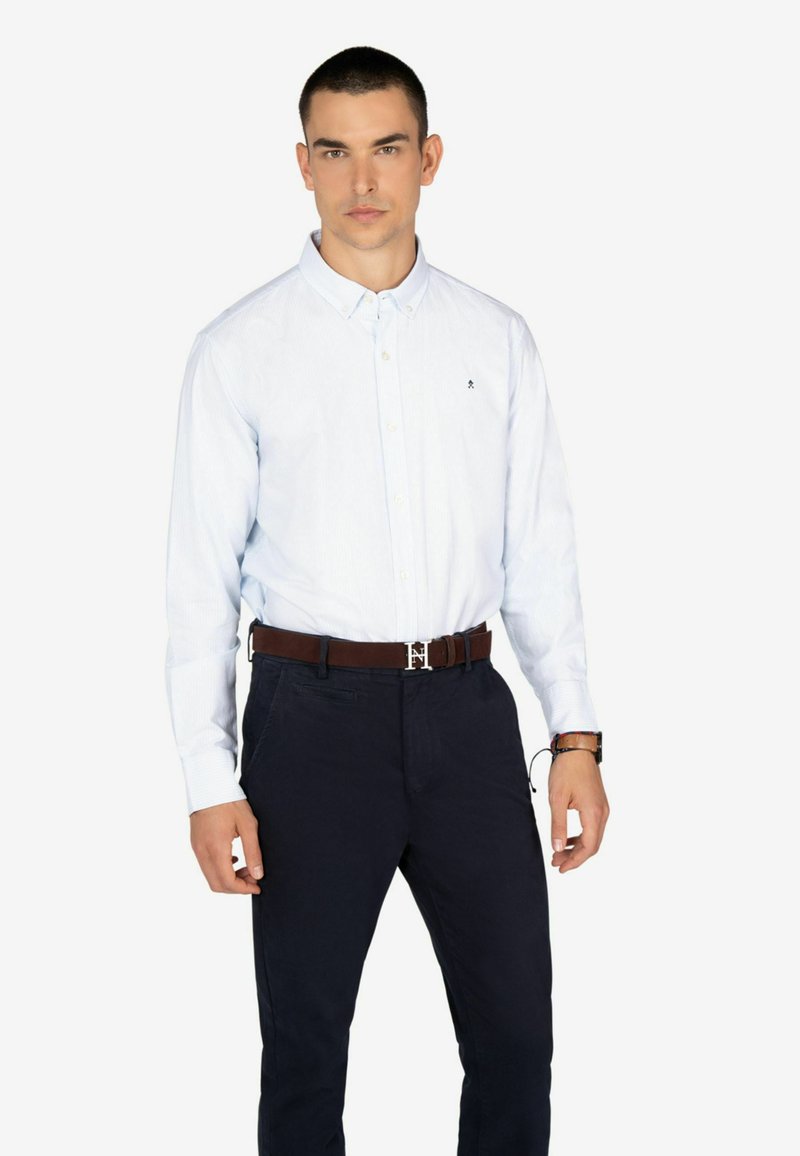 Camisa de botón a rayas azul claro con cuello, combinada con pantalones azul marino oscuros y un cinturón marrón con una hebilla de plata.