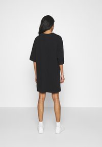 Svart oversized t-shirt klänning i bomull med korta ärmar och rundad halsringning, med en rak fåll som sträcker sig till mitten av låret.