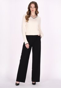 Maglione crema con scollo a V e bordo nero, abbinato a pantaloni neri a gamba larga con vita alta. Tessuto liscio; parte superiore aderente, silhouette inferiore rilassata.
