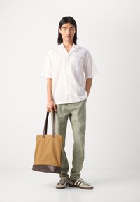 Button-up white short-sleeve shirt, green linen pants, brown and tan tote bag, brown and beige sneakers with stripes, smooth fabric texture.