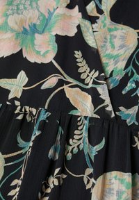 Tissu noir avec un motif floral pastel doux en vert, rose et beige, présentant des feuilles et des pétales détaillés sur une section froncée.