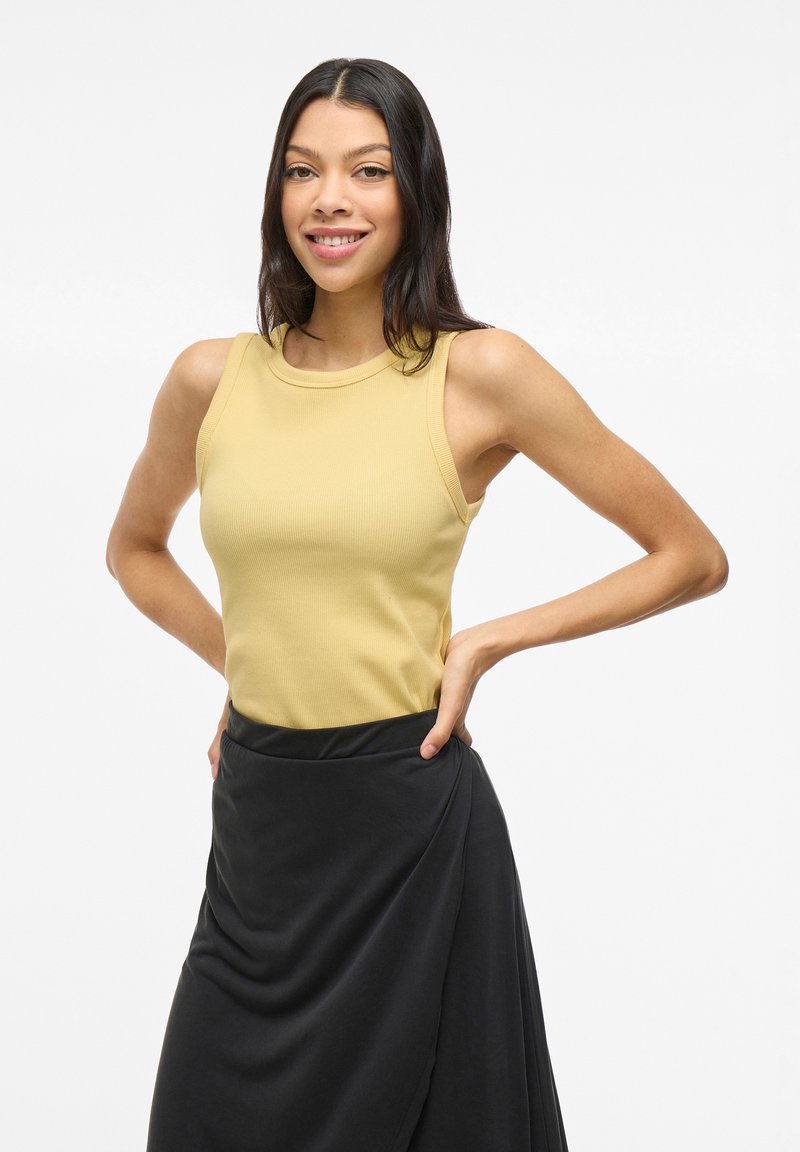 Top de tirantes acanalado amarillo combinado con una falda envolvente negra, que presenta una silueta ajustada y una textura suave. Diseño minimalista, sin patrones.