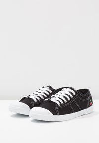 Sneaker nere in tela con lacci bianchi, punte in gomma, cuciture a contrasto e una piccola grafica di ciliegia rossa sul lato.