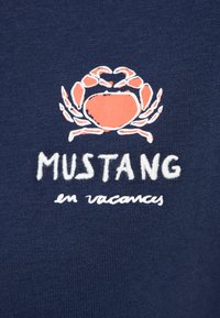 Un tissu bleu marine avec une finition texturée présente un graphique d'un crabe corail au-dessus du mot "MUSTANG" et de "en vacances" en lettres blanches brodées.