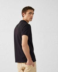 Polo shirt nero a maniche corte, con colletto classico. Indossato con pantaloni beige chiaro, che mostrano un design slim fit e dettagli minimi.