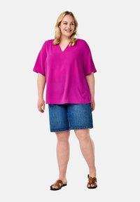 Fuchsia V-neck blouse with short sleeves paired with denim shorts. The outfit features a relaxed fit and brown sandals.