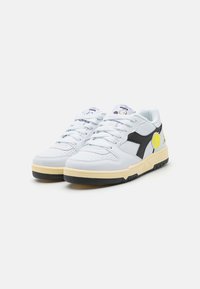 HVITE SNEAKERS MED SVARTE DETALJER, TEXTURERT LÆR, POLSTRET TUNGESNUTT, GUL TENNISBALLLOGO OG SVART GUMMISÅLE. SNØRINGSDESIGN.