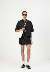 Black cropped button-up shirt over a black crop top, paired with a black mini skirt. Accessories include red sunglasses and a cream tote bag.