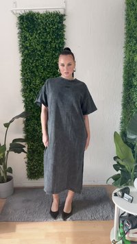Vestido midi cinza de algodão com mangas curtas, decote redondo e textura subtil. Usado com sapatos de salto alto pretos. Vegetação ao fundo.