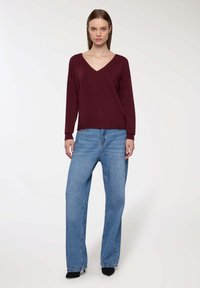 Maglione bordeaux con scollo a V e maniche lunghe, abbinato a jeans in denim blu chiaro, morbidi e a vita alta, e scarpe nere con tacco alto.