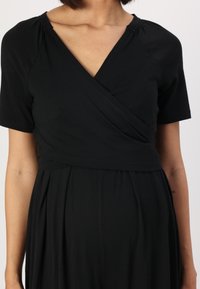 Robe noire à manches courtes, en tissu lisse. Dotée d'un décolleté en V et d'une taille froncée pour une silhouette fluide.