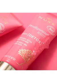 Tubo rosa della maschera detox NUXE Prodigieuse Boost, con design in foglia d'oro, cappuccio metallici lucido e consistenza in gel trasparente che fuoriesce dall'apertura.