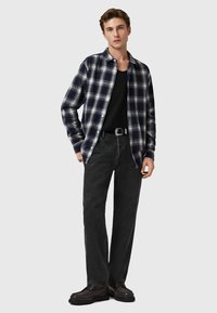 Camisa de franela a cuadros en azul marino y blanco, camiseta negra debajo, combinada con jeans negros y zapatos oscuros, con cierre de botones en la parte delantera.