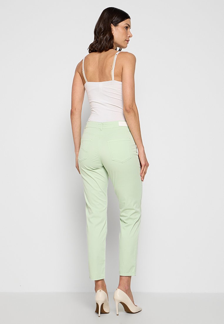 Hellgrüne Slim-Fit-Hosen mit Gesäßtaschen und schlichtem Design. Getragen mit einem weißen Tanktop und beigen High Heels.