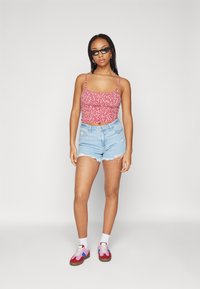 Červený kvetinový crop top s tenkými ramienkami, skombinovaný s bledomodrými roztrhnutými džínovými šortkami a viacfarebnými teniskami s bielymi ponožkami.
