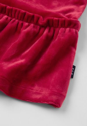 Zacht rood stof met gathered elastische details en een klein zwart merklabel op een lichtgrijze ondergrond.