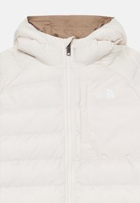 Veste isolante beige avec capuche, dotée d'une fermeture éclair complète, d'une texture matelassée et d'un petit logo blanc sur la poitrine. La doublure est marron.