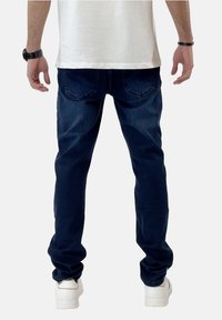 Vaqueros de mezclilla azul oscuro con un ajuste slim, diseño de cinco bolsillos y detalles de costura sutiles. Combinados con zapatillas blancas.