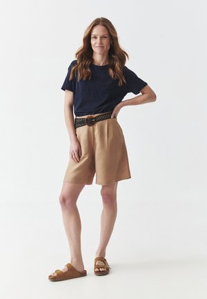 Camiseta de algodón navy con diseño bordado, pantalones cortos caqui, cinturón negro trenzado con hebilla redonda marrón y sandalias marrones. Ajuste simple y relajado.