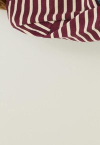 Tissu rayé bordeaux et crème, avec une apparence douce et texturée, plié de manière décontractée sur un fond clair.