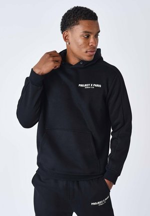 Schwarzer Hoodie mit Kängurutasche, auf der Brust mit weißem Text "PROJECT X PARIS MEMBERS' CLUB". Gerippte Bündchen und Saum.