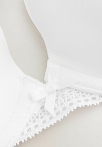 Witte beha met gladde stof, kantdetails en een klein strikje in het midden. Het ontwerp heeft voorgevormde cups en verstelbare schouderbanden.
