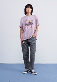Camiseta morada con el gráfico "ROXY" y montañas, combinada con pantalones grises de corte holgado y zapatillas clásicas azules. Diseño simple y casual.