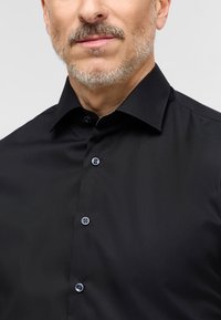 Schwarze Hemdbluse mit strukturiertem Kragen, ausgestattet mit blauen Knöpfen, glatter Textur und taillierter Passform. Wichtige Details sind die Knopfleiste.