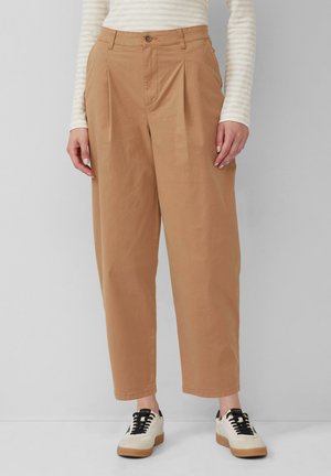 Beige, high-waisted trousers with pleats, tapered leg, and cuffed hems. Paired with white and black sneakers, creating a casual look.
