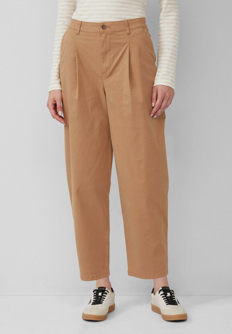 Pantaloni beige a vita alta con pieghe, gamba affusolata e orli risvoltati. Abbinati a sneakers bianche e nere, creano un look casual.