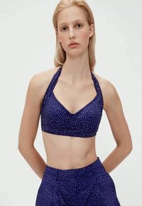 Bordo halter bralet s uzorkom točkica i V-izrezom, s prilagođenim siluetom i glatkom tkaninom. Ukrašen kontrastnim uzorkom točkica.
