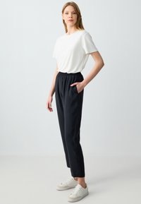 T-shirt blanc à manches courtes associé à un pantalon noir à taille élastique et des baskets blanches. Les pantalons sont dotés de poches latérales et d'une coupe décontractée.