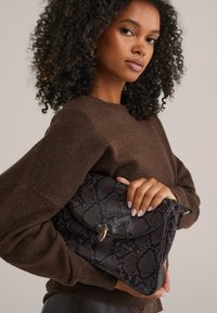 Svart och brun mönstrad handväska i strukturerat material, med en vikbar design och detaljer i guld.