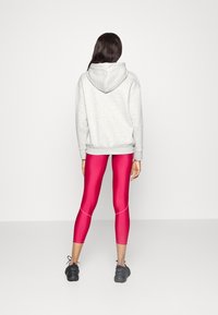 Grå hoodie med snörning, rosa leggings med kontrastsömmar, och svarta träningsskor, sedd från baksidan.