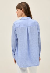 Light blue and white striped shirt, featuring long sleeves, a buttoned cuff, a back pleat, and a soft textured fabric.