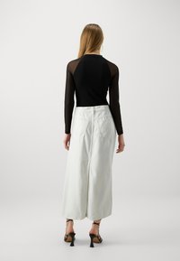 Haut noir à manches longues avec des manches transparentes, associé à une jupe en denim blanche taille haute avec poches arrière et coupe droite.