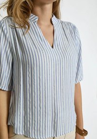 Blusa leggera a maniche corte con scollatura a V, strisce verticali blu e bianche, e una leggera lucentezza nella texture del tessuto.