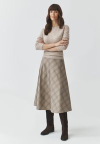 Beige Wollpullover mit Dreiviertelärmeln, kombiniert mit einem hellbraunen karierten A-Linien-Rock und braunen Wildleder-Stiefeln bis zum Knie.