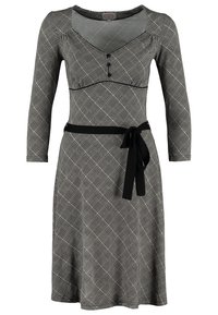 Svartvit rutigt klänning med trekvartsärmar, V-ringning, knappdetaljer och ett kontrasterande svart midjebälte.