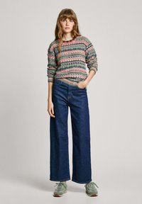 Pull en tricot avec des rayures horizontales multicolores, associé à un jean ample bleu marine et des baskets vert clair. Tissu texturé, style décontracté.