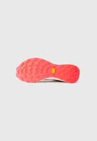 Fényes piros cipőtalp mély barázdákkal és középen egy sárga Vibram logóval, sima fehér háttérrel.
